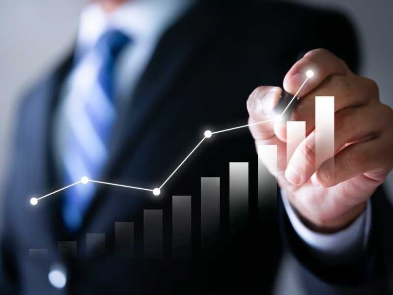 Businessperson in suit drawing an upward trending bar graph with a marker, representing growth and success.