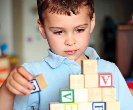 Child playing with colorful alphabet blocks, carefully stacking them on a table in a brightly lit room.